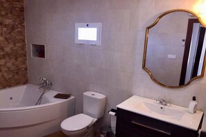 Un baño con bañera, inodoro, lavabo y un espejo con marco dorado.