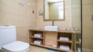 A bathroom with a toilet, a sink, and shelves with towels. - Yugang Zhizun Hotel (Dalian)