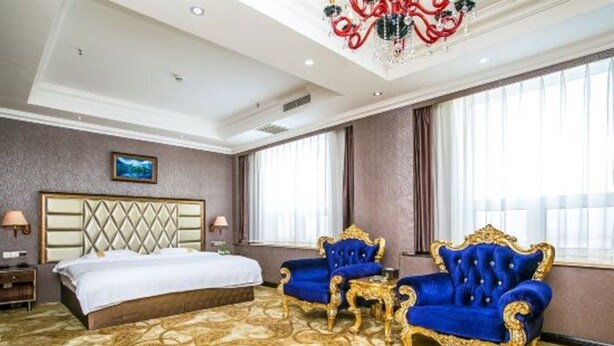 A spacious hotel room with a large bed, two blue upholstered chairs, a small table, and a chandelier. - Yugang Zhizun Hotel (Dalian)