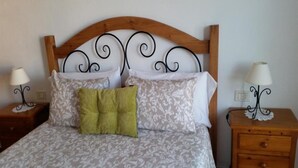 Una cama con cabecera de madera, dos mesitas de noche con lámparas y un almohadón verde.