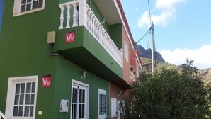 Un edificio de dos pisos con fachada verde, balcones blancos y tejado rojo.