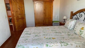 Un dormitorio con cubrecama floral, armario de madera y mesita de noche con lámpara.