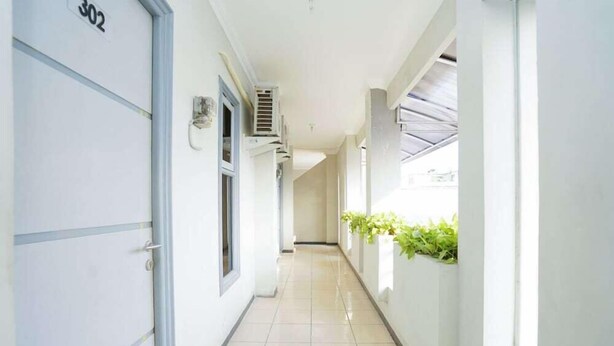 A corridor with a door labeled "302", a wall-mounted air conditioning unit, and a window with blinds. - OYO 2075 Graha Marina (Surabaya)