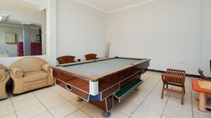 Una mesa de billar en una sala con un sofá color crema y una pequeña mesa de madera.