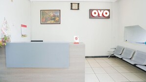 A reception area with a reception desk, a clock, a framed painting, and a sign that reads "OYO". - OYO 2075 Graha Marina (Surabaya)