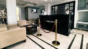 A lobby with a reception desk, seating area, and a decorative column. - Hotel Des Beaux Arts (Algiers)