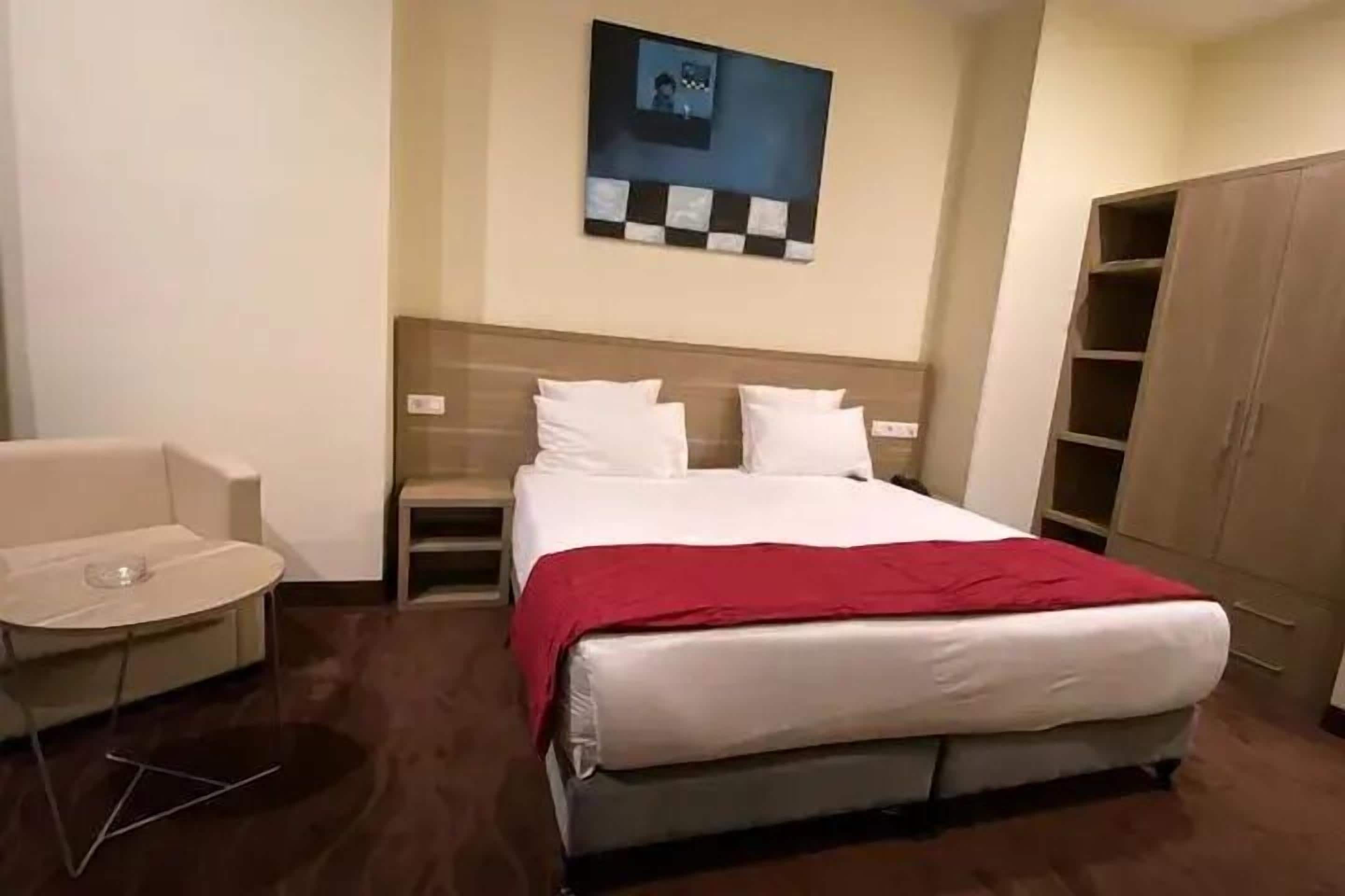 A hotel room with a bed, a chair, a table, and a wardrobe.