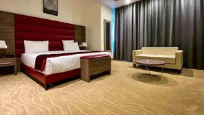 A hotel room with a large bed, a sofa, a small table, and a large window with curtains. - Hotel Des Beaux Arts (Algiers)