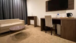 A hotel room with a sofa, a coffee table, a desk with a chair, a flat-screen TV, and a fireplace. - Hotel Des Beaux Arts (Algiers)