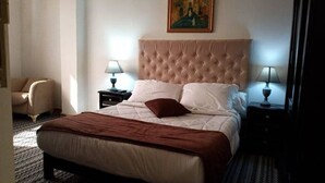 A hotel room with a large bed, two bedside tables with lamps, a chair, and a painting on the wall. - Costa Ayaa Appart Hotel (Algiers)