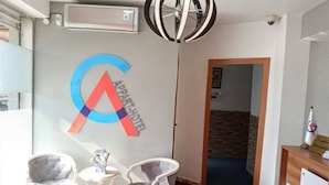 A hotel reception area with a logo on the wall, two chairs, a small table, and a reception desk. - Costa Ayaa Appart Hotel (Algiers)