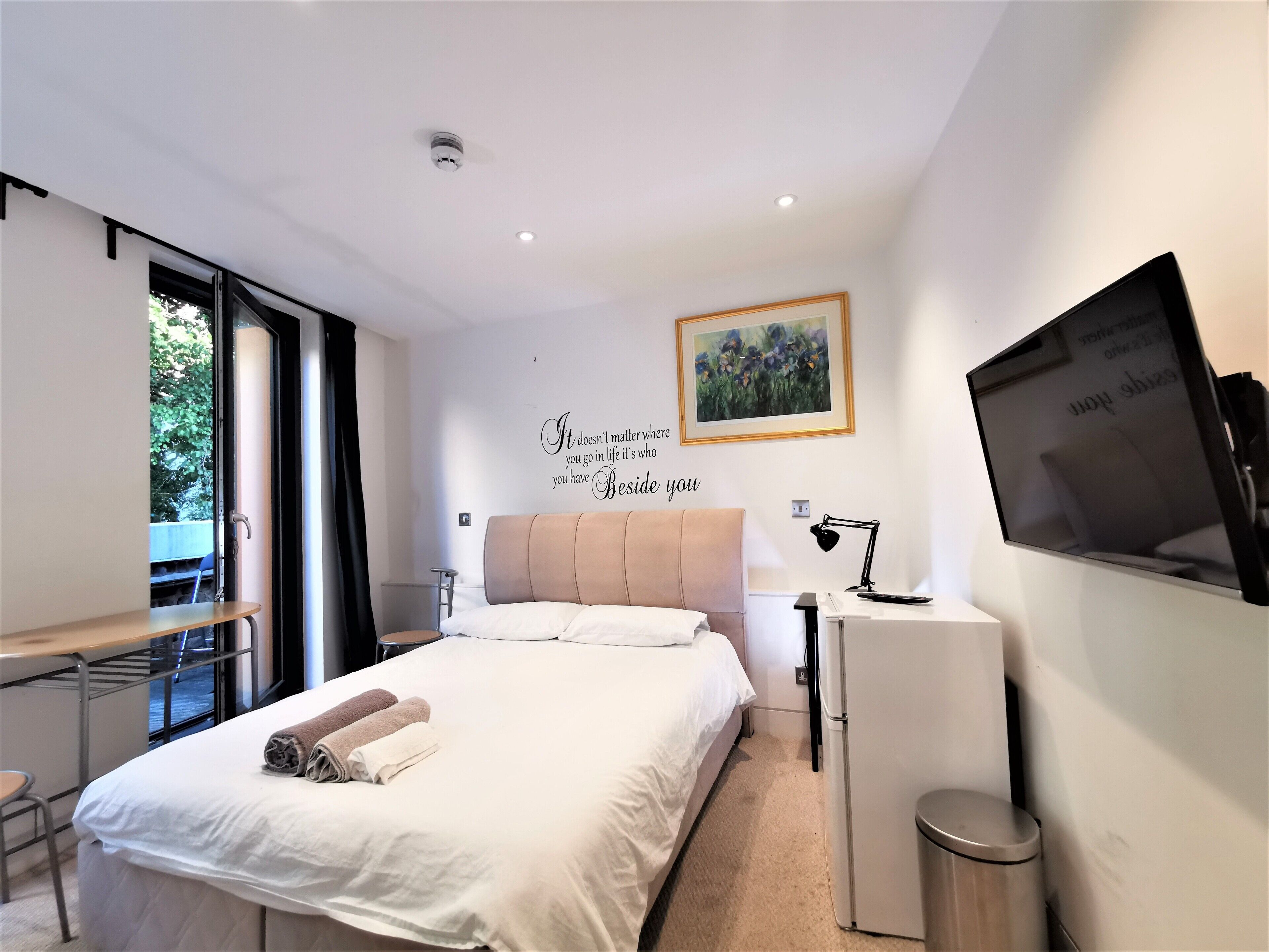 A modern bedroom with a bed, a desk, a chair, a TV, and a small table.