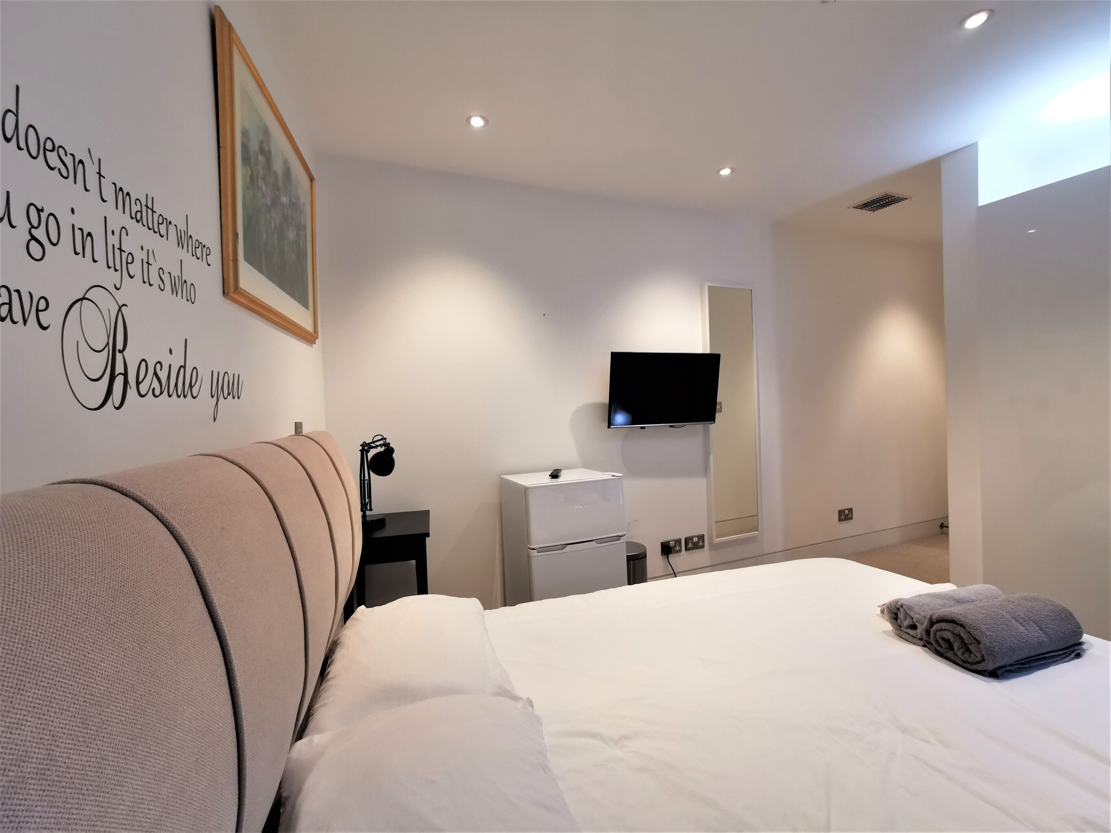 A modern hotel room with a bed, a desk, a flat-screen TV, and a wall with motivational text.