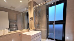 Ein modernes Badezimmer mit einer gläsernen Duschkabine, einem großen Spiegel und einem weißen Waschtisch.