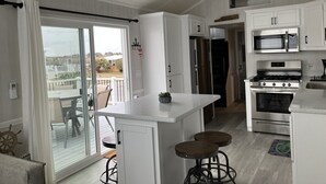 Une cuisine moderne avec des meubles blancs, un réfrigérateur en acier inoxydable, un four encastré et un four à micro-ondes. Une porte-fenêtre coulissante donne accès à un balcon aménagé avec du mobilier d’extérieur.