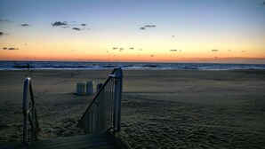 Une plage avec une promenade en bois menant à l’eau, une rambarde et quelques poubelles.