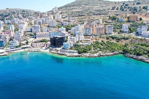 An aerial view of a coastal town with buildings along the shoreline and a clear blue sea. - Apartments Romario Sarande (Sarandë)