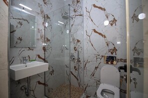 A bathroom with a marble backsplash, a glass shower enclosure, a white sink, and a toilet. - Apartments Romario Sarande (Sarandë)