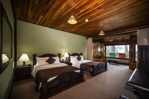Une chambre d’hôtel avec deux lits, un plafond en bois et une grande fenêtre donnant sur la forêt.