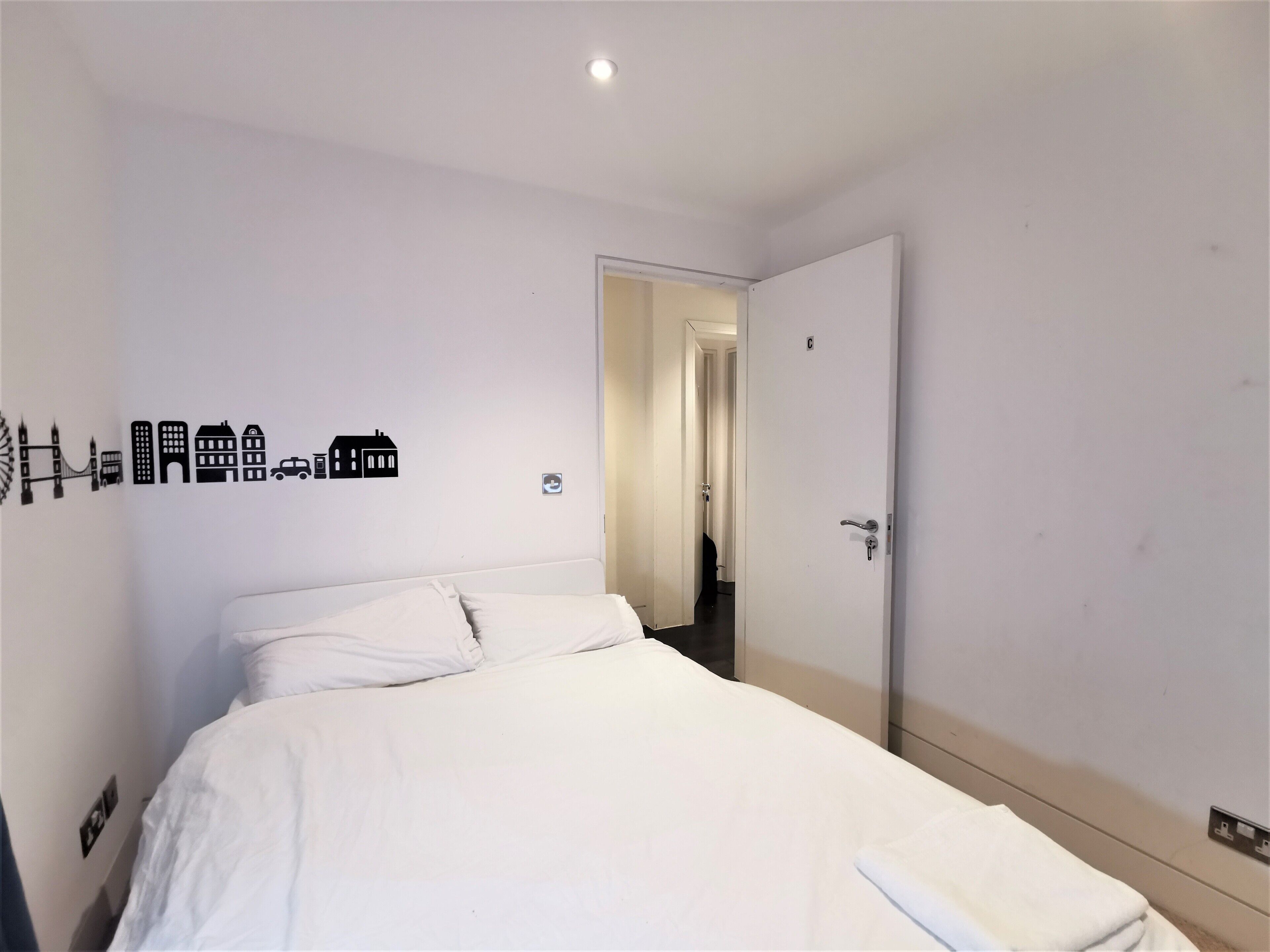 A hotel room with a bed, a door, and a wall with a cityscape decal.
