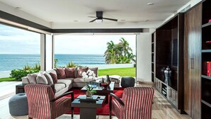A modern living room with a large sofa, striped armchairs, a coffee table, and a view of the ocean. - Private Luxury Escape, Cabo San Lucas Villa 1048 (Cabo San Lucas)