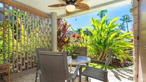 Un patio con dos sillas y una mesa, rodeado por una valla de madera y exuberante vegetación tropical.