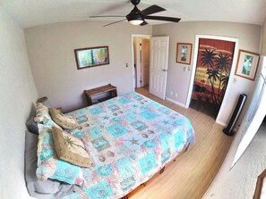 Una camera da letto con un letto, una ventola a soffitto, una porta e un quadro appeso al muro.