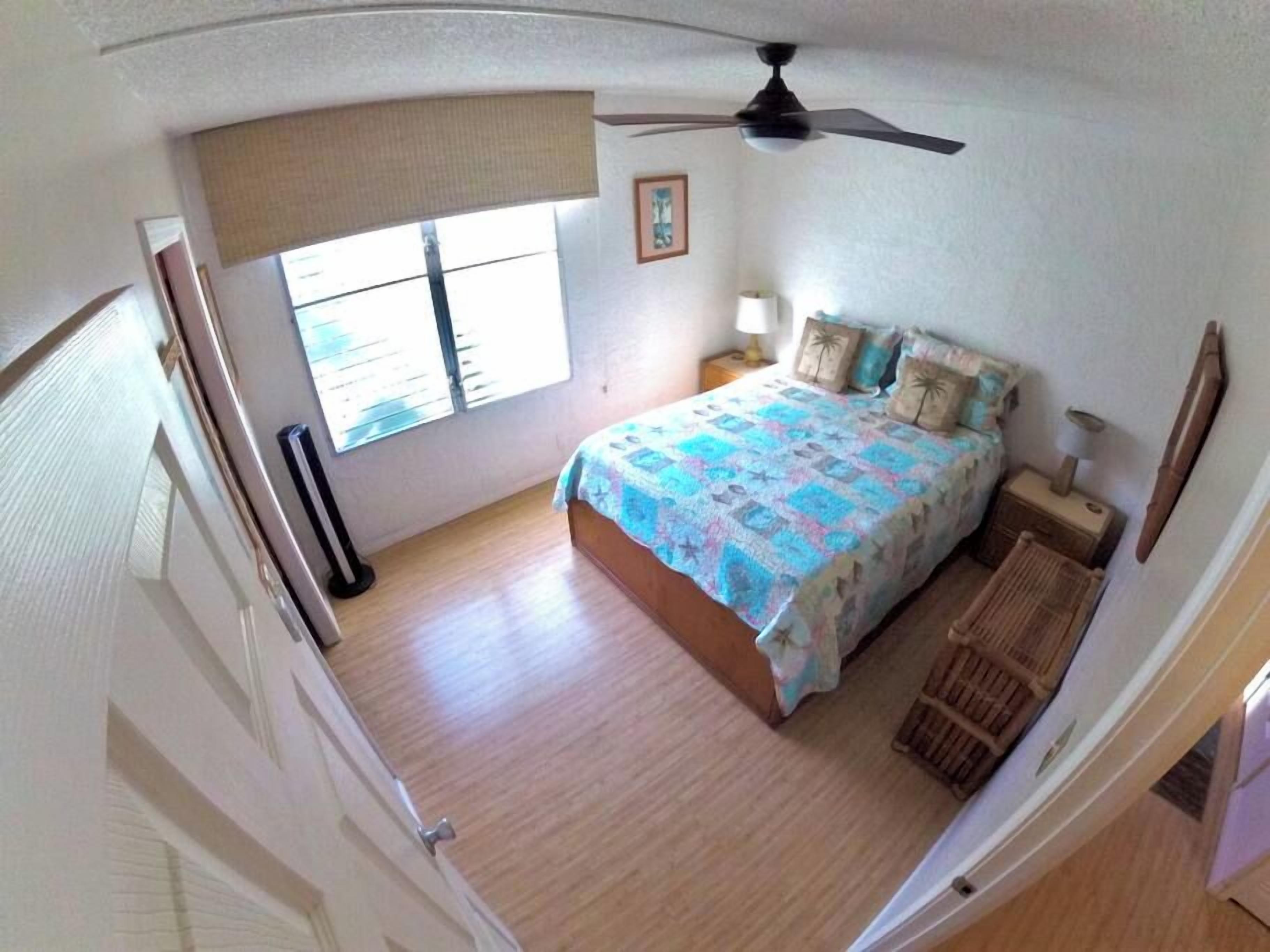 A bedroom with a bed, a ceiling fan, a window, and a nightstand.