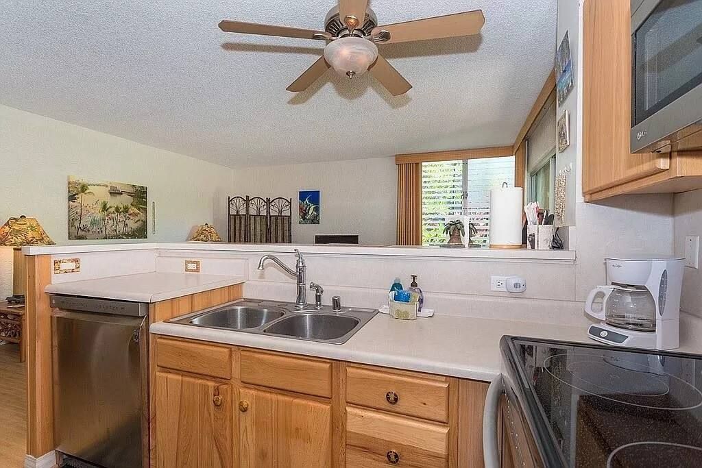 A compact kitchen with wooden cabinets, a built-in dishwasher, a double sink, and a ceiling fan.