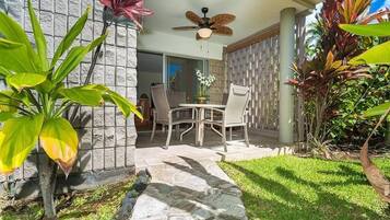 An outdoor patio with a table and chairs, surrounded by tropical plants and a stone pathway.