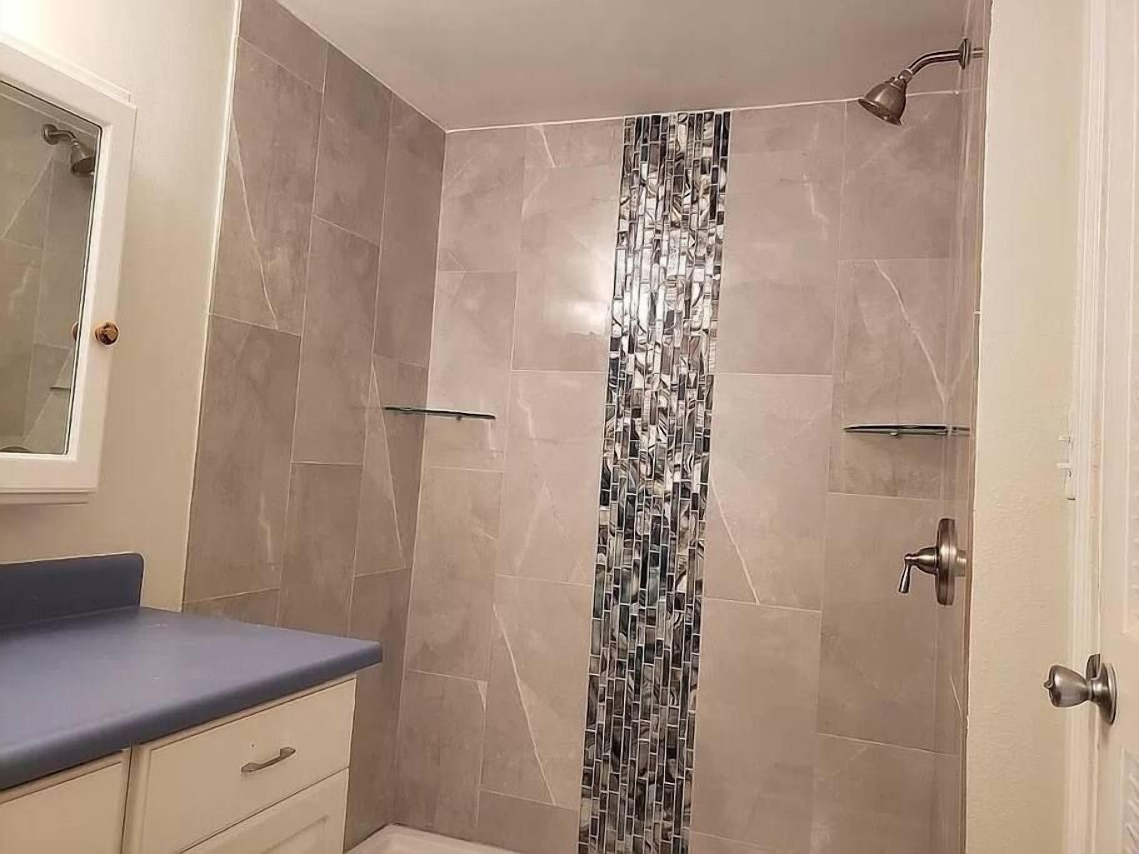 A bathroom with a shower, a mirror, and a vanity with a blue countertop.