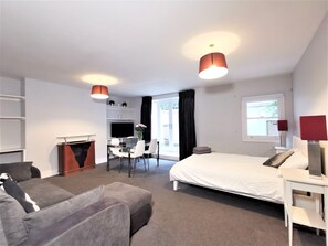 A modern hotel room with a bed, a desk with a chair, a sofa, a TV, and a window with curtains. - Spacious 2 bed flat in Camden (London)