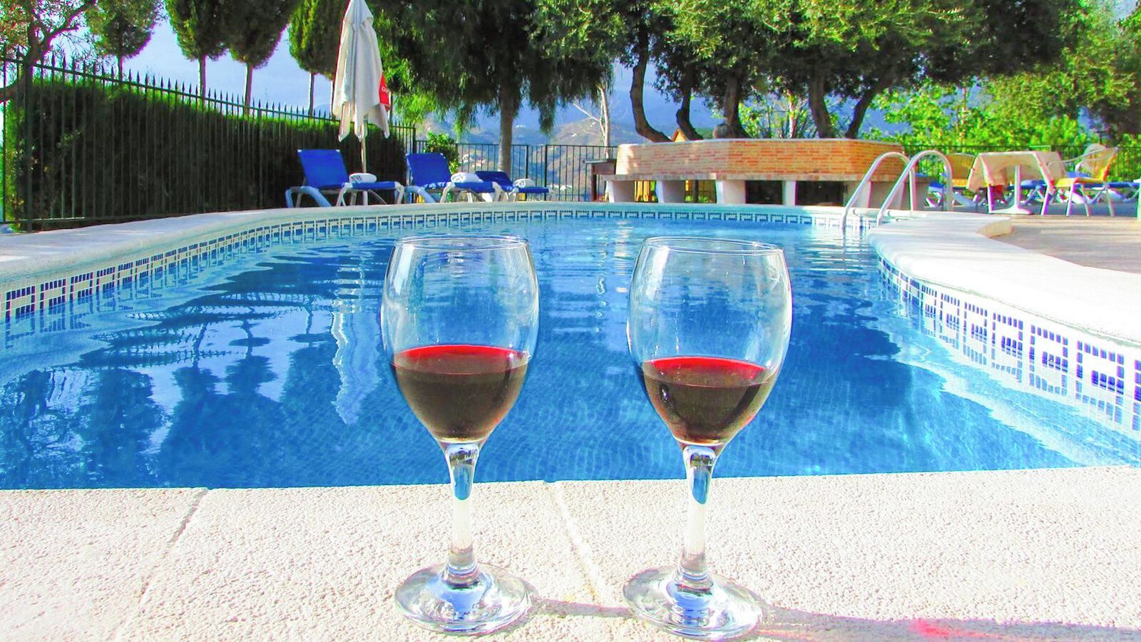 A swimming pool with two glasses of red wine on the edge.