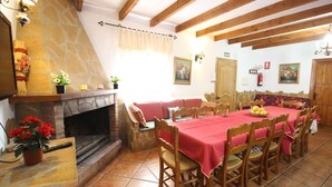A dining area with a stone fireplace, wooden beams, and a table set for six. - Parador de los Olivos Sayalonga by Ruralidays (Málaga)