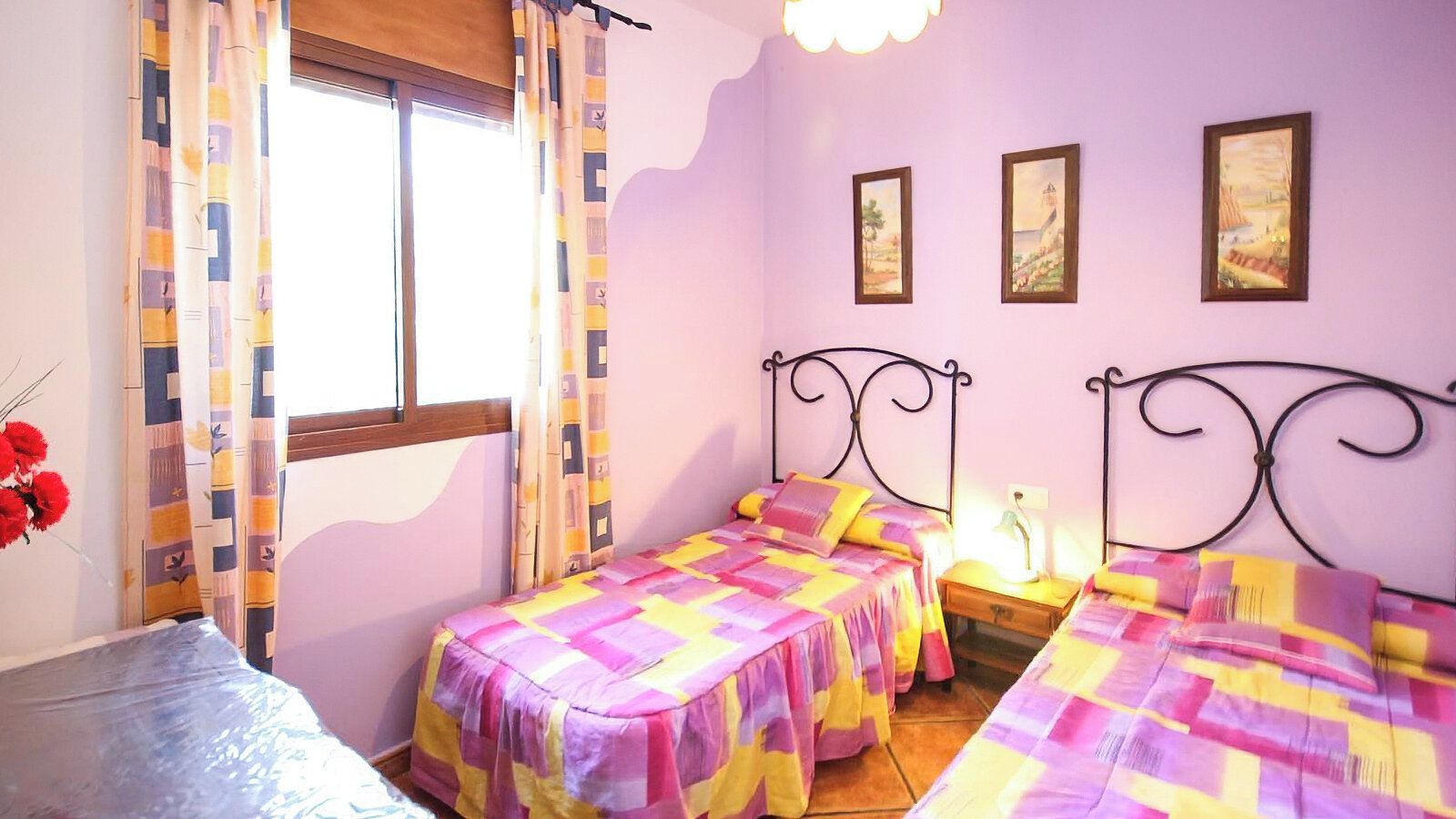 Une chambre avec deux lits, une fenêtre avec des rideaux et des tableaux accrochés au mur.