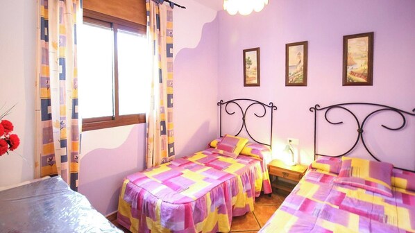 A room with two beds, a window with curtains, and wall-mounted pictures.