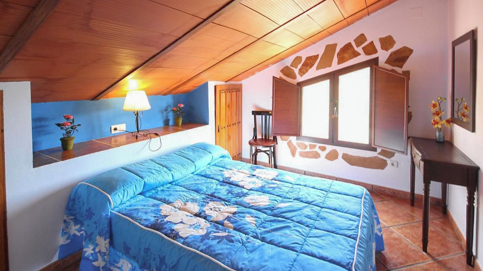 A bedroom with a bed, a desk, a chair, a lamp, and a window.