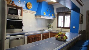 A kitchen with a blue countertop, a microwave, an oven, and a sink. There is a fruit bowl on the counter. - Parador de los Olivos Sayalonga by Ruralidays (Málaga)