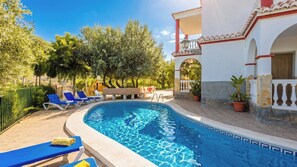 A swimming pool with lounge chairs, a stone wall, and a building with a balcony.