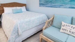 Un dormitorio con cama, cabecera de madera, sofá azul y una pared con un cuadro de una ola gigante.