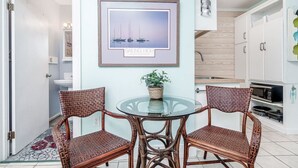 Un comedor con sillas de mimbre, una mesa de vidrio y un cuadro con barcos a vela en la pared.