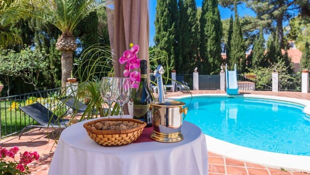 A poolside table with a bottle, glasses, and a bowl of nuts. - Finca Mi Hogar Málaga - Churriana by Ruralidays (Málaga)