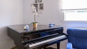 A black piano with a blue chair in front, a small table with a teapot and a plant, and a window with blinds. - Finca Mi Hogar Málaga - Churriana by Ruralidays (Málaga)