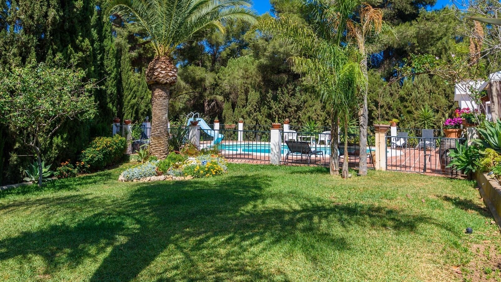 Un jardin à l’arrière de la maison, avec une piscine, entouré d’une clôture et agrémenté de différentes plantes.