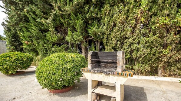 A barbecue grill with a tiled seating area, surrounded by potted plants and dense greenery. - Sortes Ana Órgiva by Ruralidays (Granada)