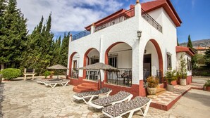 A building with a white facade and red accents, featuring a patio with lounge chairs and umbrellas. - Sortes Ana Órgiva by Ruralidays (Granada)