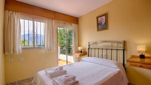 A hotel room with a bed, a nightstand, a lamp, a window with curtains, and a painting on the wall. - Sortes Ana Órgiva by Ruralidays (Granada)