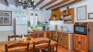 A kitchen with wooden cabinets, a microwave, and a dining table set with bread and vegetables. - La Monja Antequera - La Higuera by Ruralidays (Málaga)