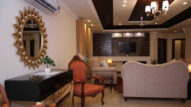 A living room with a black console table, a red upholstered chair, a beige sofa, and a large gold-framed mirror. - Homewood Suites (Lahore)