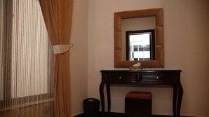 A room with a wooden desk, a mirror, a window with curtains, and a trash bin. - Homewood Suites (Lahore)